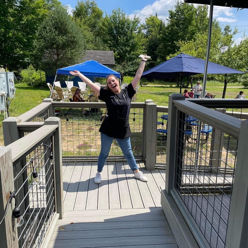 A Chef Darrell's Mountain Diner employee joyfully stands on an outdoor deck with arms raised.