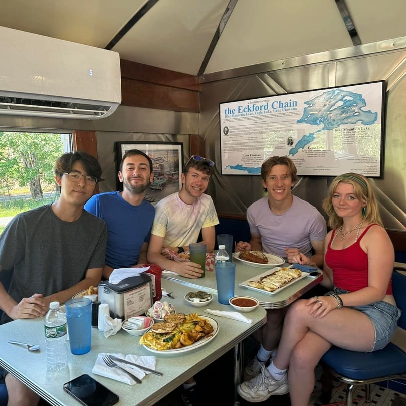 Five young adults enjoying diner food and drinks at a booth in Chef Darrell's Mountain Diner.