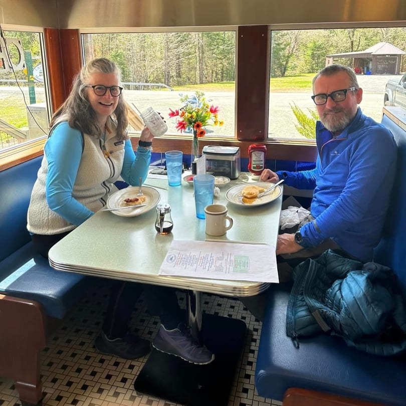 Two happy diners enjoying breakfast pancakes and coffee in a blue booth at Chef Darrell's Mountain Diner.