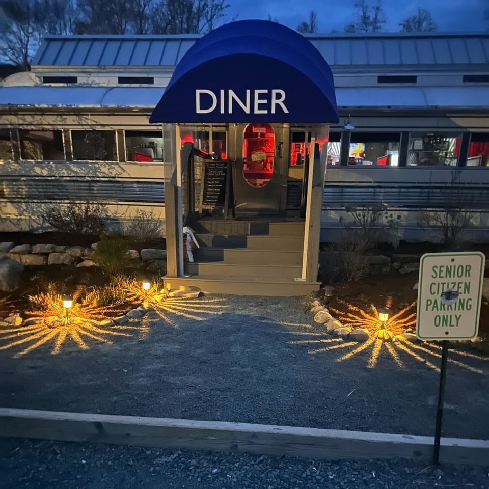 Chef Darrell's Mountain Diner exterior at dusk, with a blue awning, red interior lights, and illuminated path.