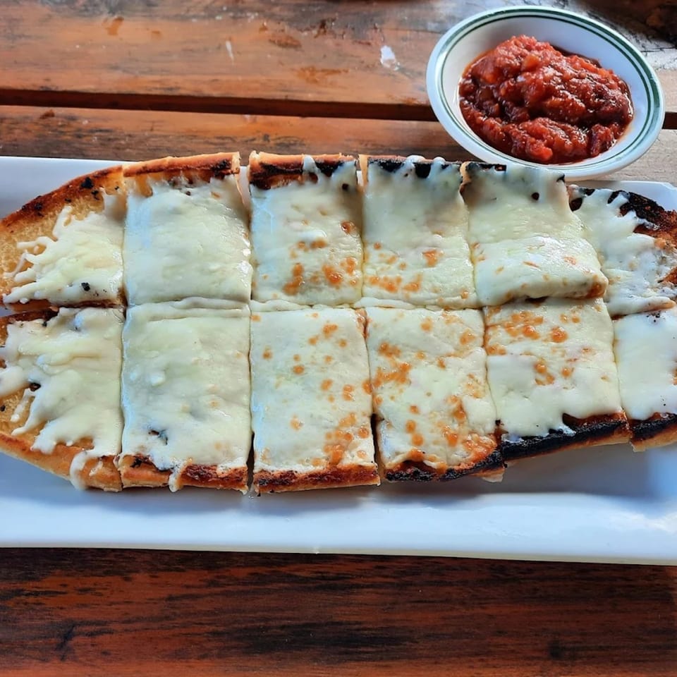 Cheesy garlic bread, cut into squares, served with a side of marinara sauce on a wooden table.
