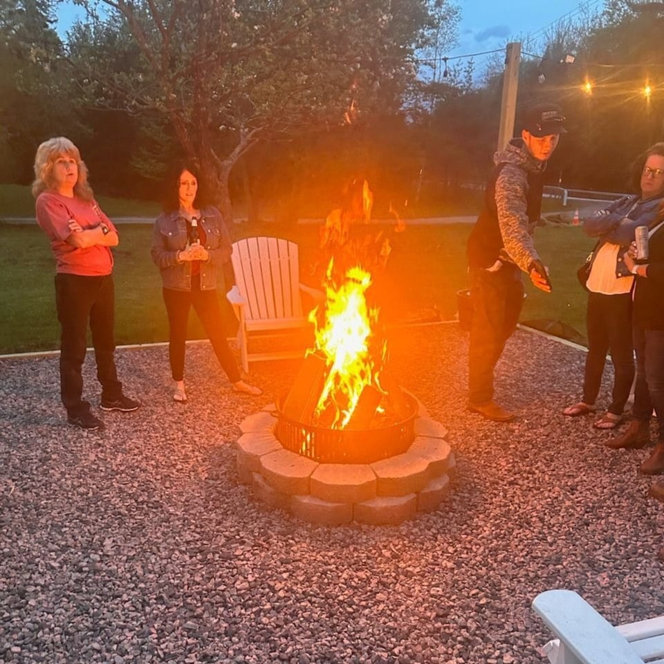 Diner guests gather around a fire pit on a gravel patio at dusk, enjoying the outdoor ambiance.