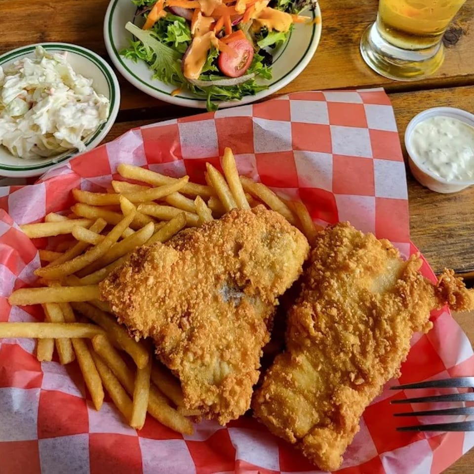Fish and chips in a red checkered basket, with coleslaw, salad, and a drink.