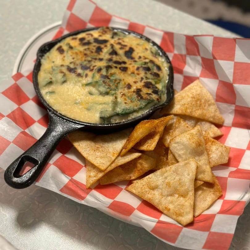 Spinach dip in a cast iron skillet with crispy tortilla chips on a red and white checkered liner.
