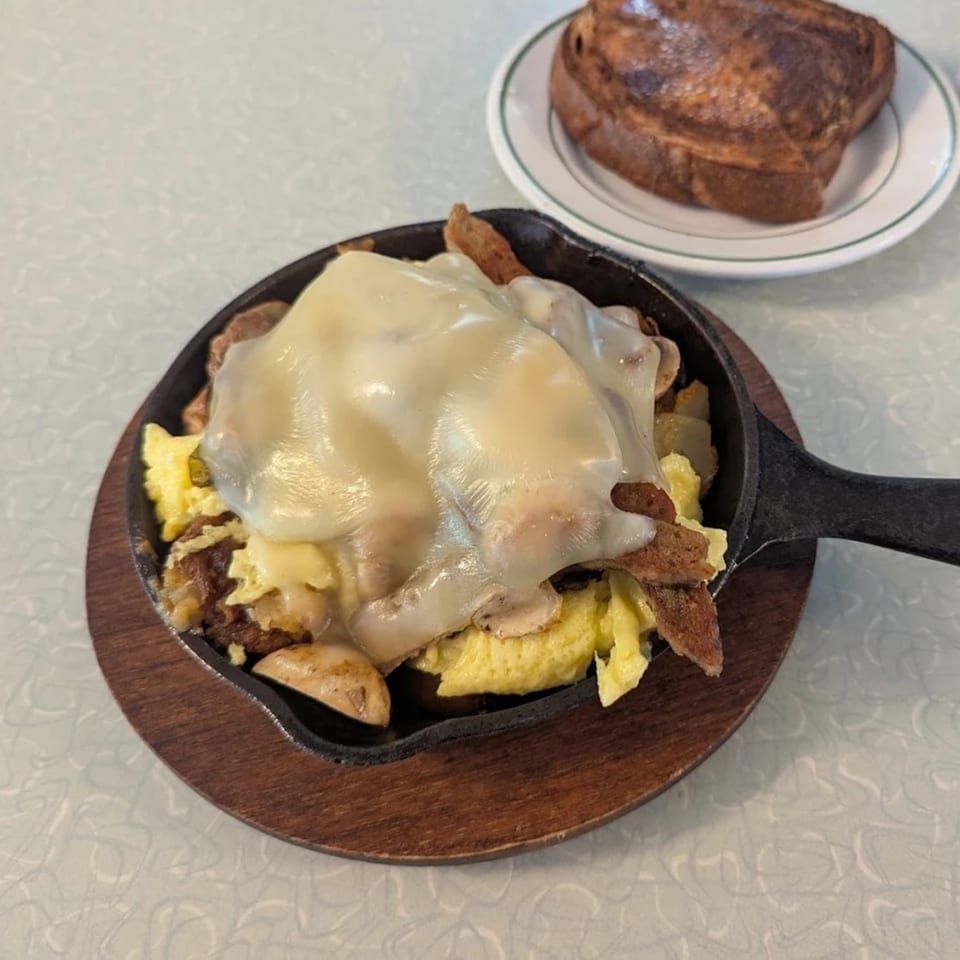 Skillet breakfast with melted cheese, scrambled eggs, and meat, served with French toast.