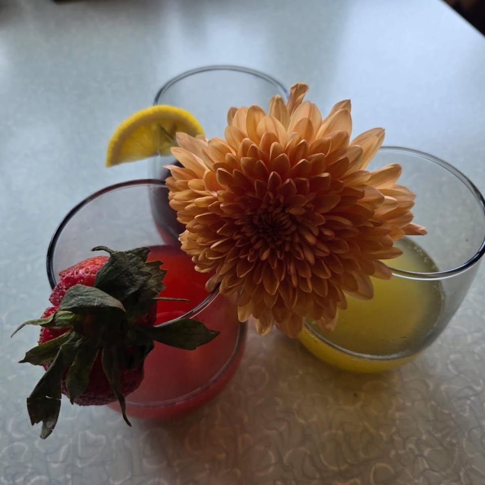 Three drinks on a table, one with a strawberry, one with a lemon, and one with a flower.