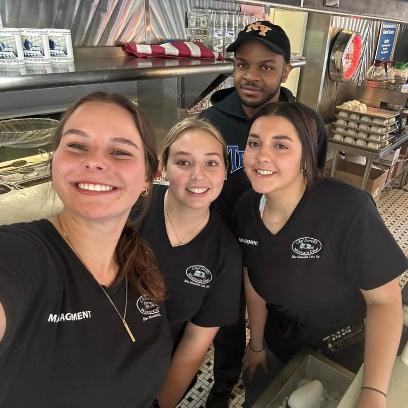 Four smiling Chef Darrell's Mountain Diner staff members, three women and one man, stand behind the counter.