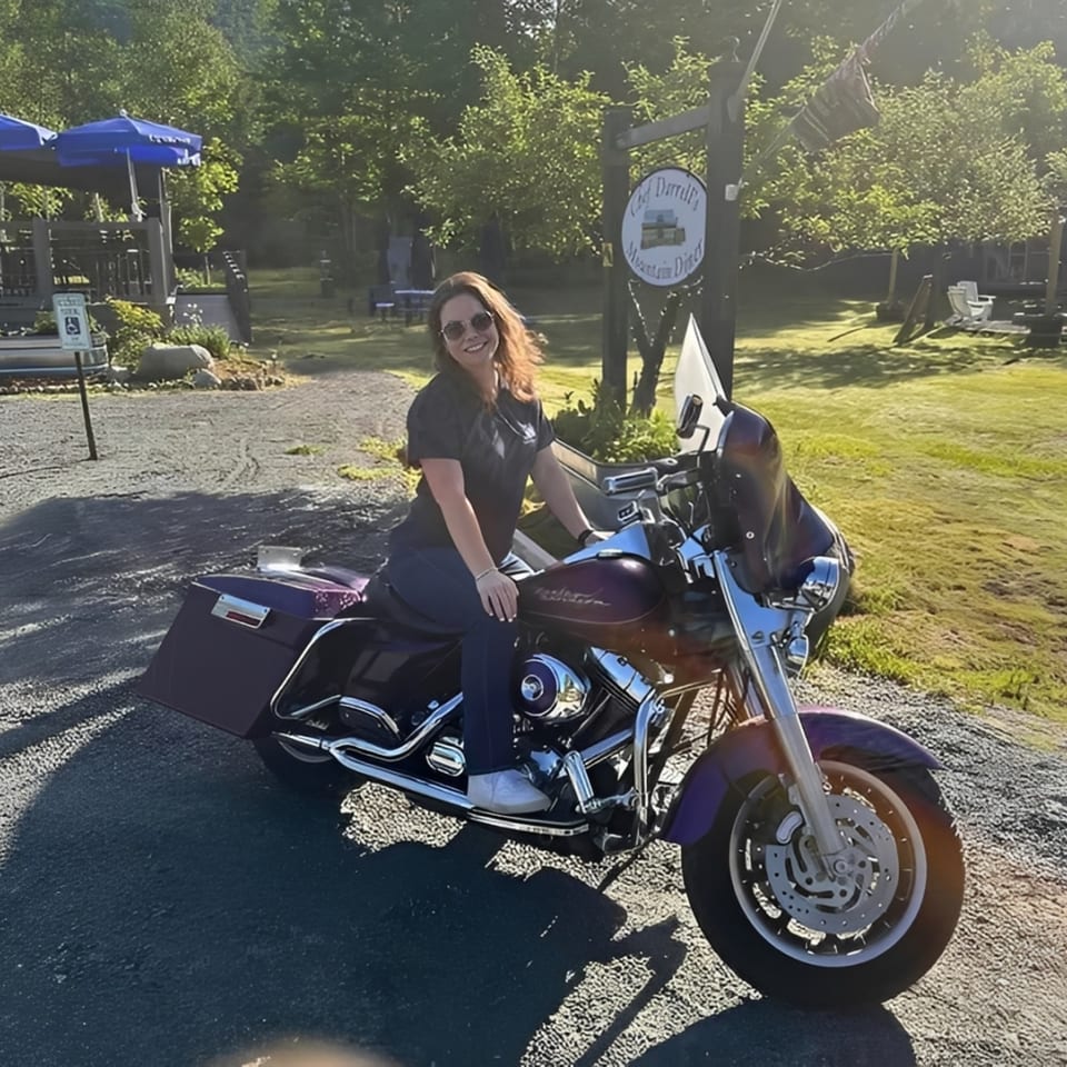 A woman in sunglasses sits on a purple motorcycle in front of Chef Darrell's Mountain Diner.