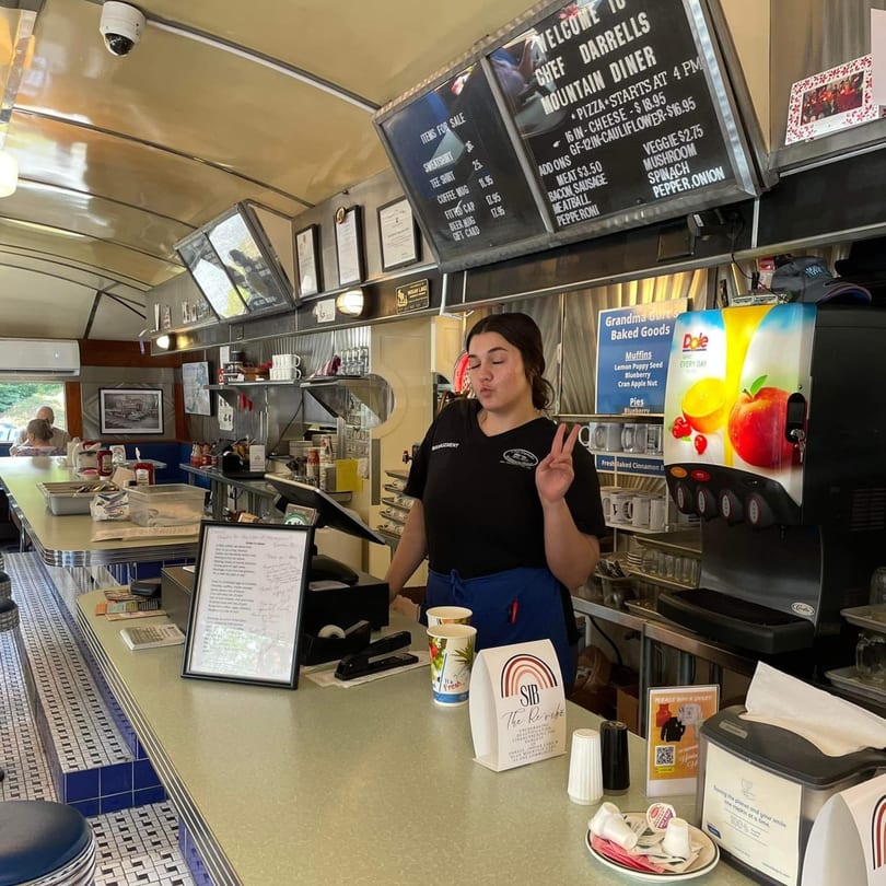 A server at Chef Darrell's Mountain Diner stands behind the counter, making a peace sign.