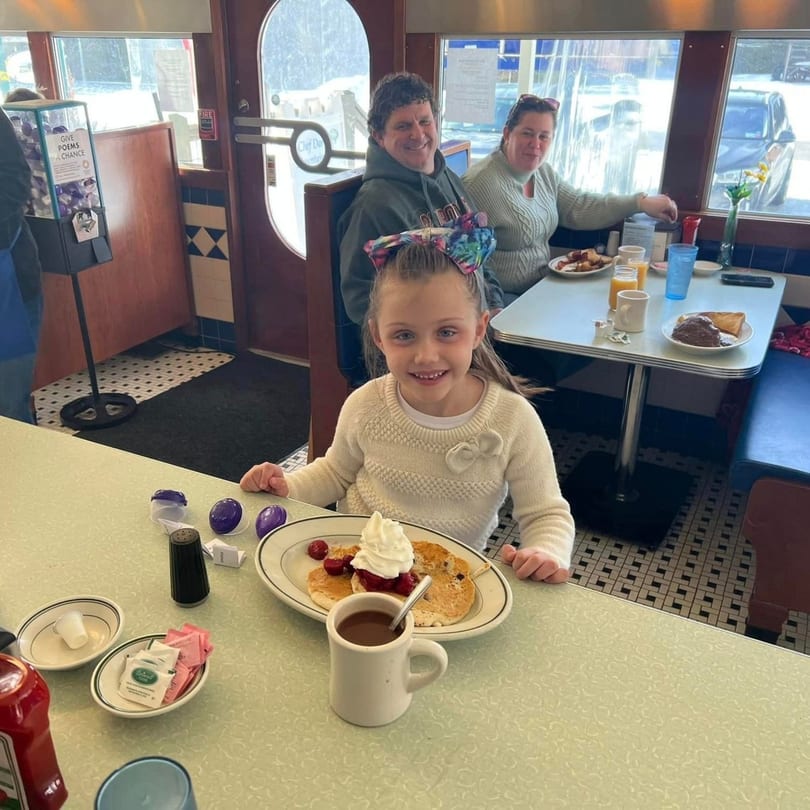 A young girl smiles at the camera with pancakes and hot chocolate at Chef Darrell's Mountain Diner.