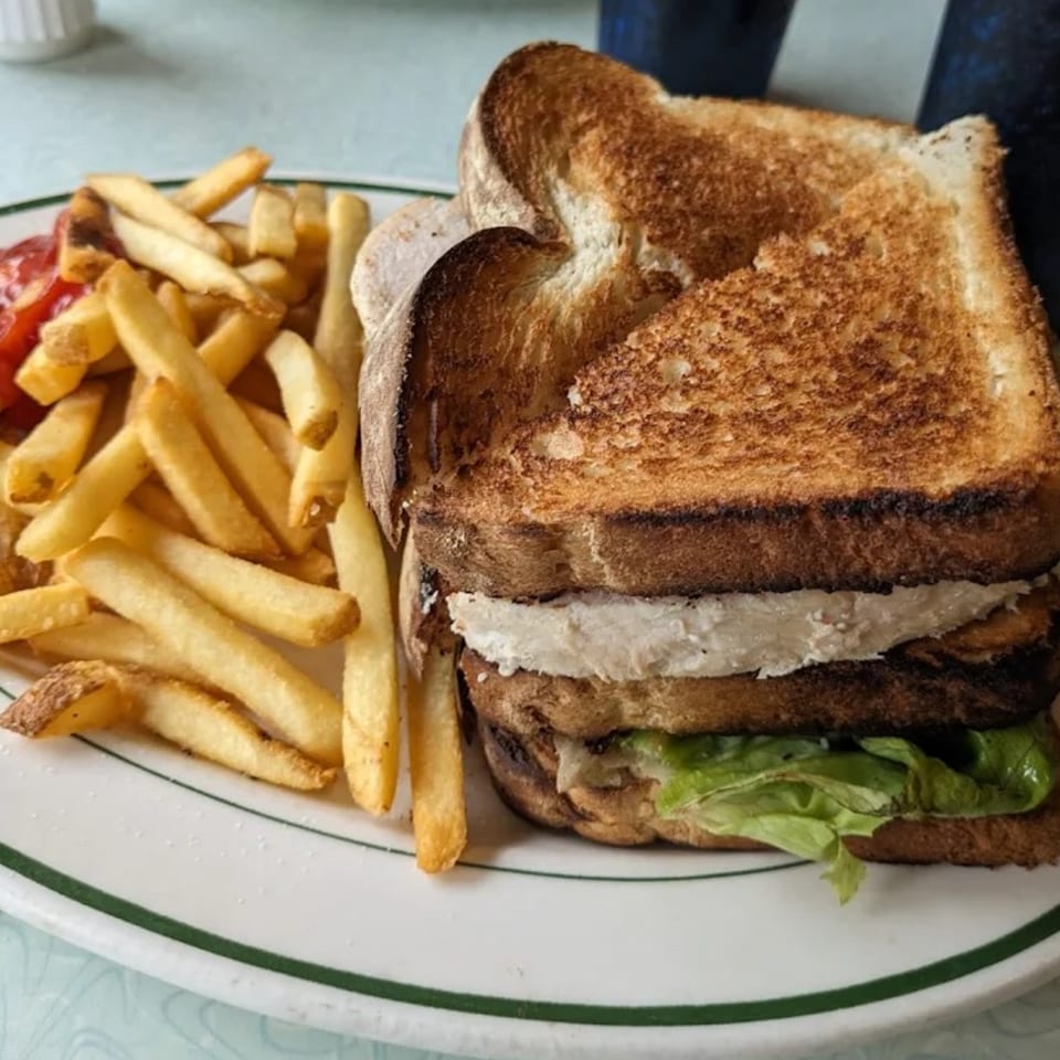 A diner-style club sandwich with fries and ketchup on a white plate with a green rim.